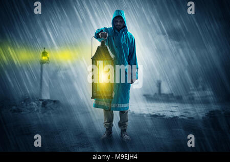 Man at the coast coming in raincoat with glowing lantern concept  Stock Photo