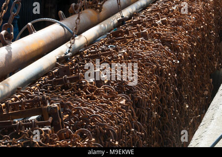 Chain mat, used for raking the sea-bed to disturb scallops, nephrops and flatfish from sediment, hanging over the edge of a fishing trawler boat. Stock Photo