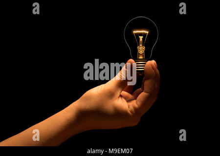 Hand holding a filament lamp on a black background. The bulb as a symbol of an idea. Glowing tungsten bulb. Ecological concept. Stock Photo