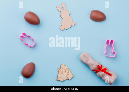 Chocolate eggs and rabbits, top view. Chocolate Easter eggs, papercut rabbits and molds on blue background with copy space in the center. Stock Photo