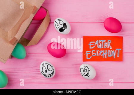 Easter egg hunt. Easter eggs with different facial expressions and paper bag. Dyed eggs and card with text Easter egg hunt. Stock Photo