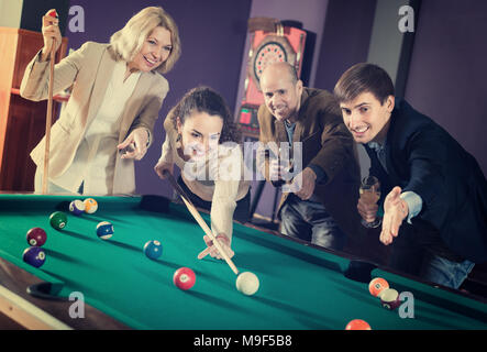Joyful smiling young and mature couples playing pool in billiard club . Selective focus Stock Photo