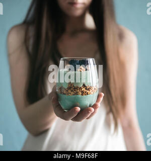 Triffle dessert in woman hands. Blue spirulina and fruit smoothie with granola, blueberry and blackberry in glass. Healthy detox food and breakfast idea and recipe. Stock Photo