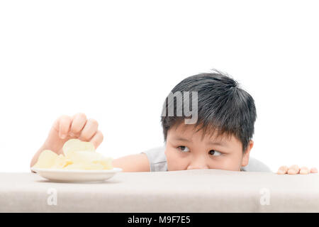 Obese fat boy is reaching  potato crisps on table isolated on white background, unhealthy and junk food concept Stock Photo