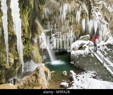 Happy celebrating winning success man standing on bridge with arms raised up above his head in enjoying icicles and waterfall on winter hike with rais Stock Photo