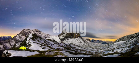 Panorama of illuminated tent under starry night sky in snowy alpine mountains. Alps, Switzerland. Stock Photo