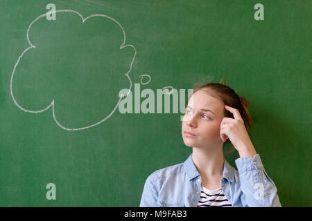 Student thinking blackboard concept. Pensive girl looking at thought bubble on chalkboard background. Caucasian student. Stock Photo