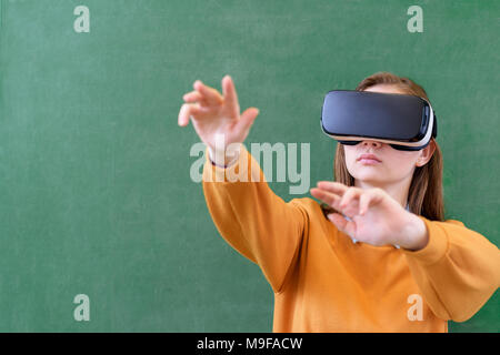 Teenager female student wearing virtual reality glasses in classroom at school. Innovative teaching methods. Education concept. Stock Photo