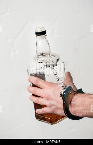 Young man at living room alcohol problems holding bottle of whiskey locked with handcuffs close-up Stock Photo
