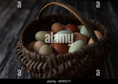 A basket of farm fresh eggs in multiple colors, on a wooden background Stock Photo