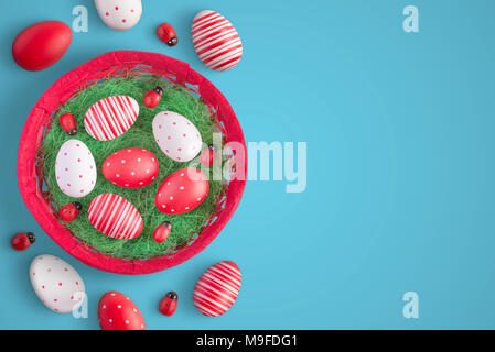 Easter eggs in red basket with ladybug decorations. Top view of blue surface with free space for text. Stock Photo