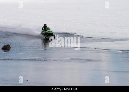 Snowmobile racing across an open patch of water on Lake Pleasant, NY in the Adirondack Mountains with copy space. Stock Photo