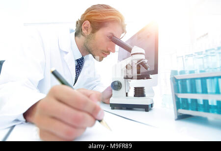 A young male lab specialist is working on some samples and takes notes in his clipboard Stock Photo