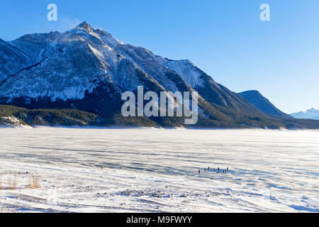 42,747.08405 snowy Abraham Lake with blue ice 9 distant photographers at work, and mountains in the background, Nordegg, Alberta Canada, North America Stock Photo