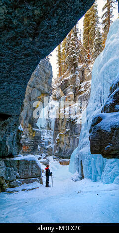 42,749.08933 Woman exploring a deep winter snowy frozen river canyon (Maligne River Canyon) looking up at frozen ice walls icefalls Stock Photo