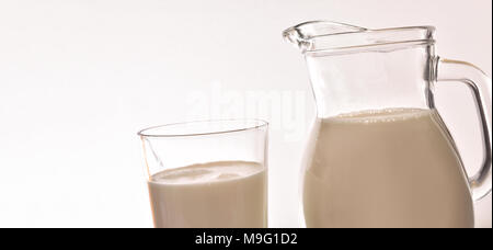 Pitcher and glass tumbler full of milk on white isolated gradient background close up. Horizontal composition Stock Photo