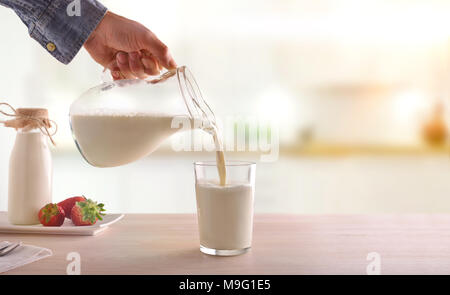 Serving breakfast milk with a jug in a glass on a white wooden kitchen table. Horizontal composition. Front view Stock Photo