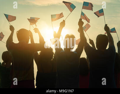 Silhouettes of people holding the flag of USA. Group of people waving american flags at sunset. Stock Photo