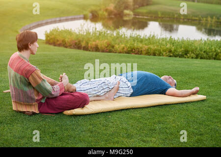 Feet thai massage outdoor. Senior man lying and relaxing on mat on the grass. Stock Photo
