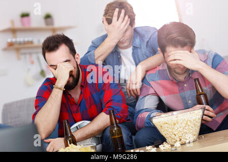 Picture of sad male friends watching sports on tv at home Stock Photo