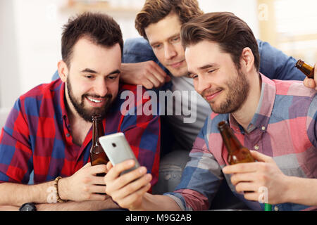 Group of friends watching smartphone sitting on a couch in the living room at home Stock Photo
