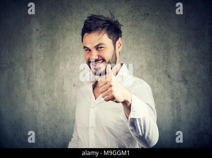 Successful young man in white shirt giving like and showing thumb up with smile. Stock Photo