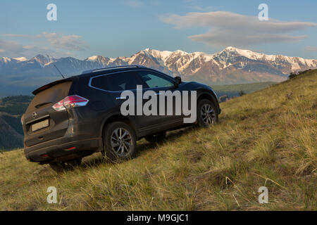 Crossover Nissan X-TRAIL on the hillside in Kurai steppe against the backdrop of the North Chuy ridge at dawn. Stock Photo