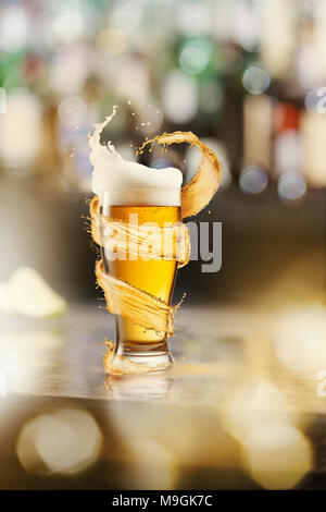 A cold glass of beer and a splash around on a blurred bar counter background Stock Photo