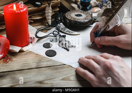 Female hand writes the letter with feather quill pen. Old books, compass, candeles on a wooden background. Stock Photo