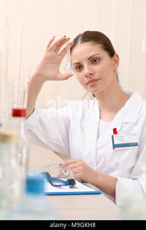 Woman lab assistant holding a empty test tube and watch closely on it. Female scientist researcher conducting an experiment in a laboratory Stock Photo