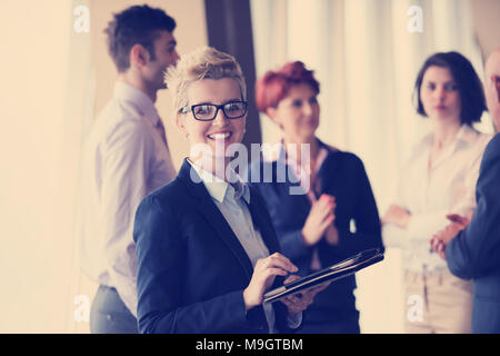 Smilling senior older  business woman with tablet computer  in front her team blured in background. Group of young business people at modern bright  s Stock Photo