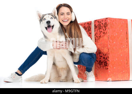 husky dog and tender woman in winter earmuffs with big christmas gift behind, isolated on white Stock Photo