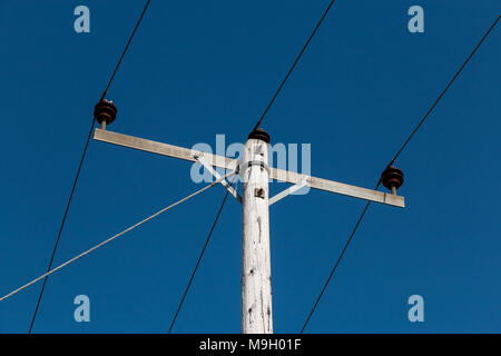 Electricity power supply pole with crossbar and 3 overhead cables attached against a deep blue sky background Stock Photo