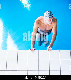 Senior man standing in water in an indoor swimming pool. Active pensioner enjoying sport. Top view. Stock Photo