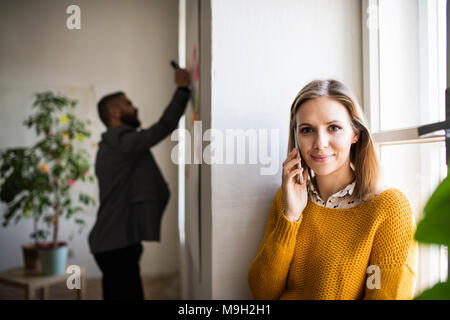 Two business people in the office working together. A woman with smartphone, making a phone call. Stock Photo