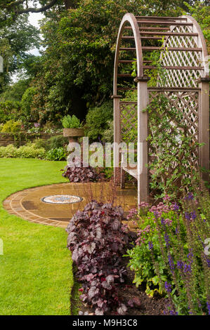 Wooden trellis seat arbour, mosaic art, lawn & summer border plants in beautiful, traditional, designed, landscaped garden - West Yorkshire, England. Stock Photo