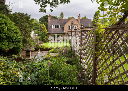 Small terraced area (stone sundial screened by trellis fence) lawn, arbour & house - beautiful, traditional, landscaped garden - Yorkshire, England. Stock Photo