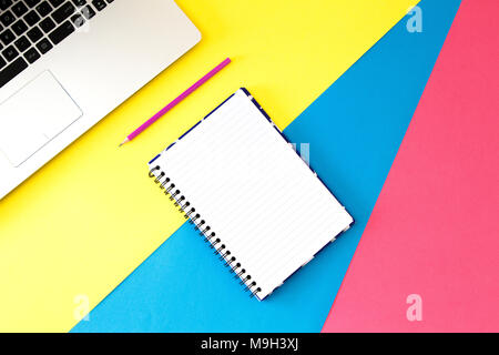 Top view office table desk. Workspace with laptop, pen and open spiral notebook page on colorful background Stock Photo