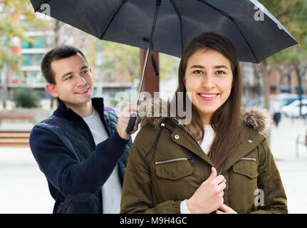 Young positive couple having a city walk and smiling in rain Stock Photo