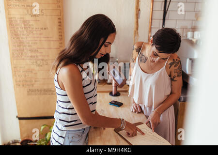 Restaurant owner helping a customer with the menu. Customer ordering food looking at the menu at the billing counter. Stock Photo