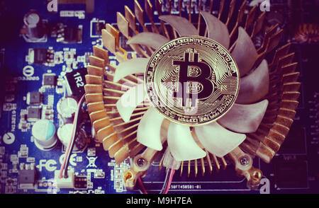 Physical Gold Bitcoin Coin on a computer video card. New independent worldwide cryptocurrency. Bitcoin mining with computer. Stock Photo