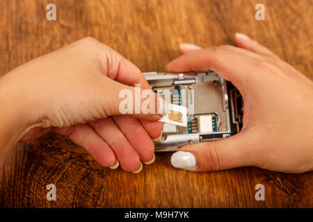 the insertion of the SIM card in a smartphone on wooden table. girl's hands insert SIM card in the phone Stock Photo