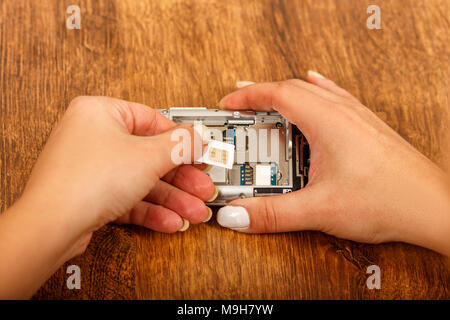the insertion of the SIM card in a smartphone on wooden table. girl's hands insert SIM card in the phone Stock Photo