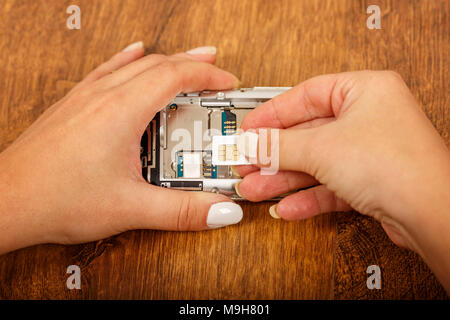 the insertion of the SIM card in a smartphone on wooden table. girl's hands insert SIM card in the phone Stock Photo