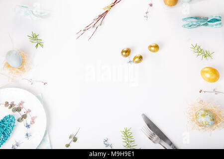 Easter table setting with gold and blue eggs and cutlery on white. Holidays background. Backdrop with copy space, flat lay, top view. Stock Photo