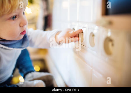 Little toddler putting fingers in a power socket. Domestic accident. Dangerous situation at home. Child safety concept. Stock Photo