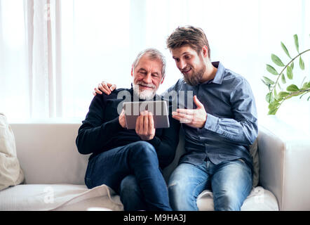 Hipster son and his senior father with tablet at home. Two generations indoors, having fun. Stock Photo