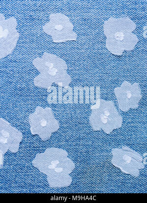 Small flowers cutted of fine white fabric, sewn randomly on blue denim. Stock Photo