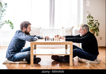 Hipster son and his senior father at home, playing chess. Two generations indoors. Stock Photo