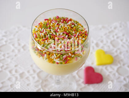 Vanilla creme in glass decorated with colored sprinkles on the top and two heart shaped cookie on the background Stock Photo